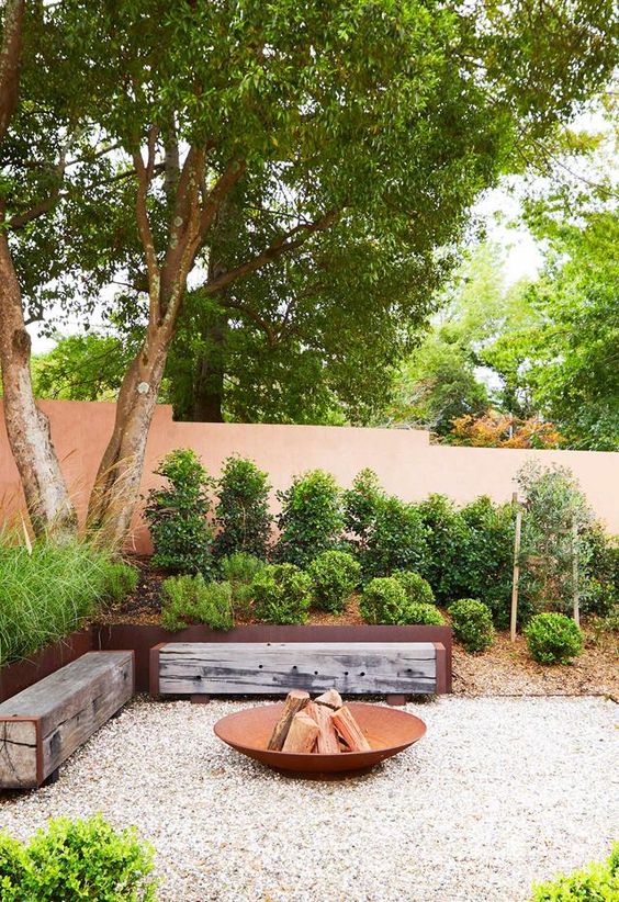 a lovely garden with an outdoor fire pit, wood slab benches and a tree over the space is very welcoming