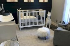 a lovely modern nursery with a black accent wall, a white dresser and crib, a grey chair and pretty artworks and decor