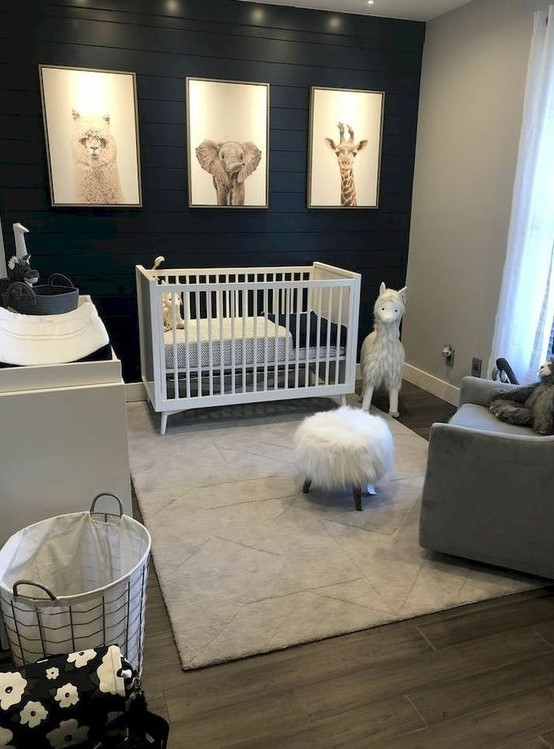 a lovely modern nursery with a black accent wall, a white dresser and crib, a grey chair and pretty artworks and decor