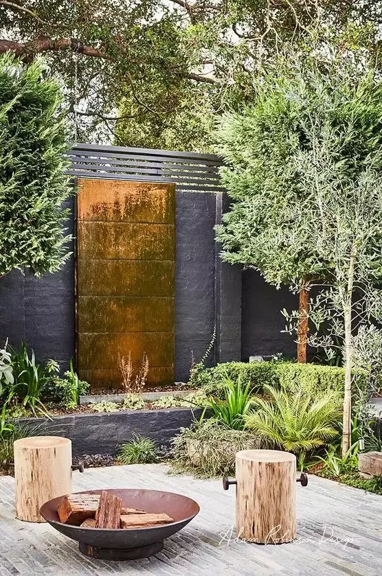 a lovely outdoor space with a copper waterfall, some greenery around, wooden stools and a metal fire bowl is amazing