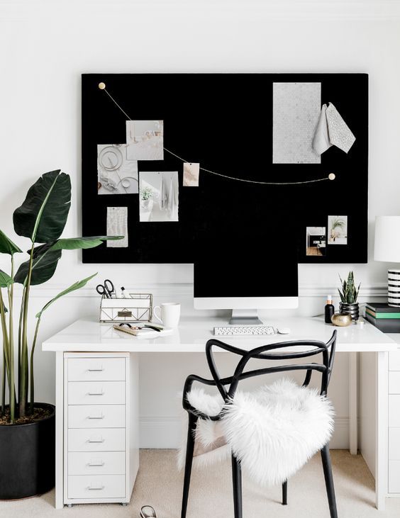 a lovely small home office in black and white, with a white desk, a black memo board, a black chair with white faux fur and a black planter with a plant