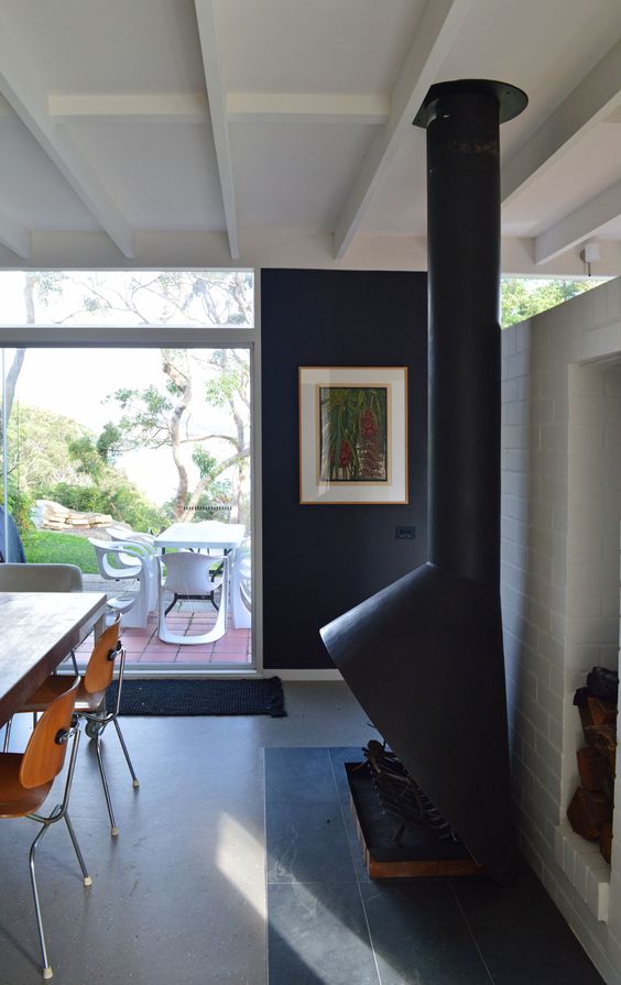 a mid century modern dining room with black walls, a black Malm fireplace, a stained table and matching chairs