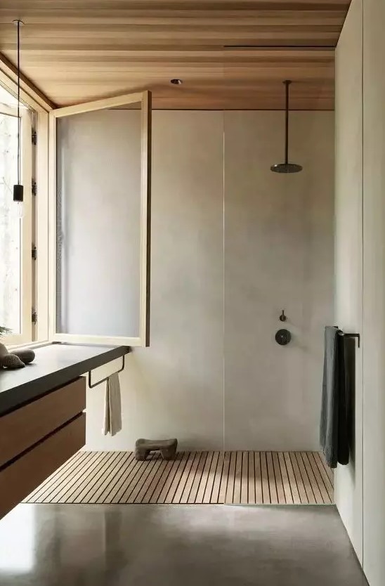 a minimalist bathroom clad with light stained wood and with concrete, with black fixtures and a vanitu with a concrete countertop