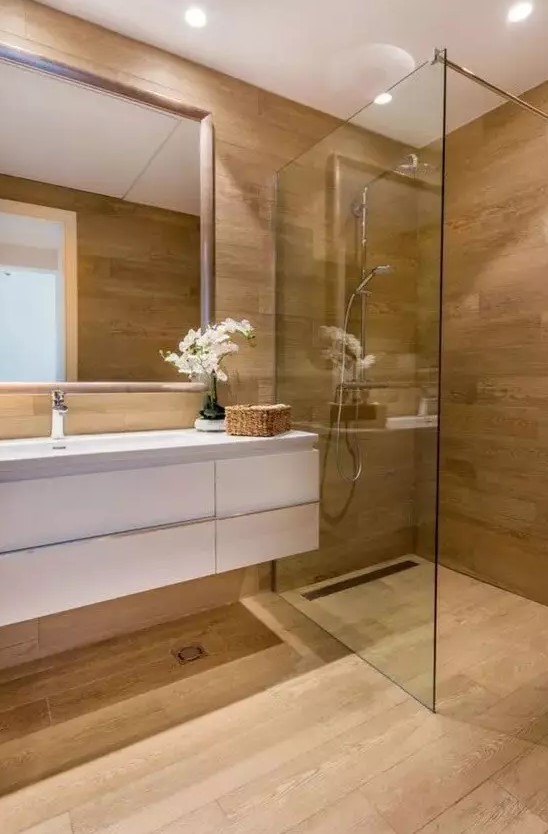 a minimalist bathroom fully clad with wood, with a glass-enclosed shower space, a floating white vanity and a mirror
