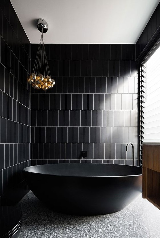 a minimalist black and gold bathroom with a stone floor, a bubble chandelier and a pretty free-standing tub