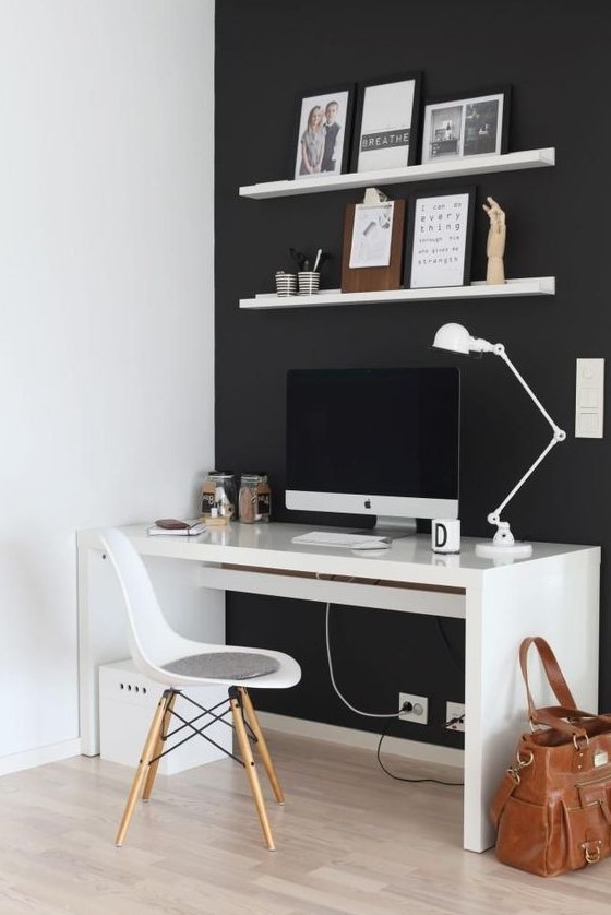 a minimalist black and white home office with a black statement wall, white furniture and some art