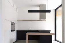 a minimalist black and white kitchen with a white storage unit and upper cabinets, black lower ones and a kitchen island with a light-stained table