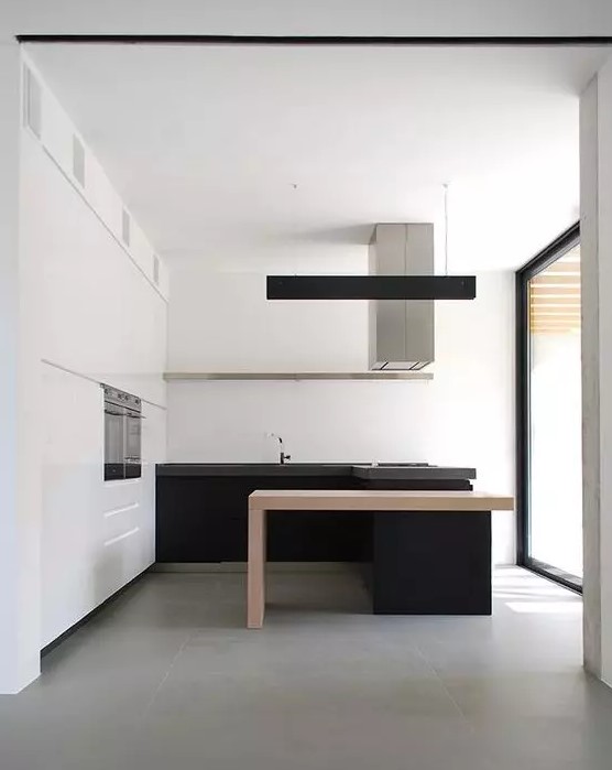 a minimalist black and white kitchen with a white storage unit and upper cabinets, black lower ones and a kitchen island with a light-stained table