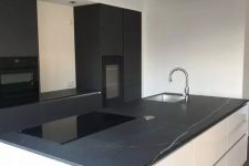 a minimalist kitchen with matte black cabinets, a large white kitchen island, black marble countertops and built-in appliances