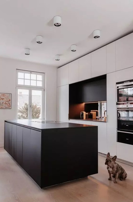 a minimalist kitchen with white cabinets and a black kitchen island, a black additional cabinet and a mirror backsplash, white lamps