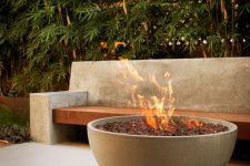 a minimalist outdoor space with a concrete and wood bench, with a large concrete fire pit filled with rocks is amazing