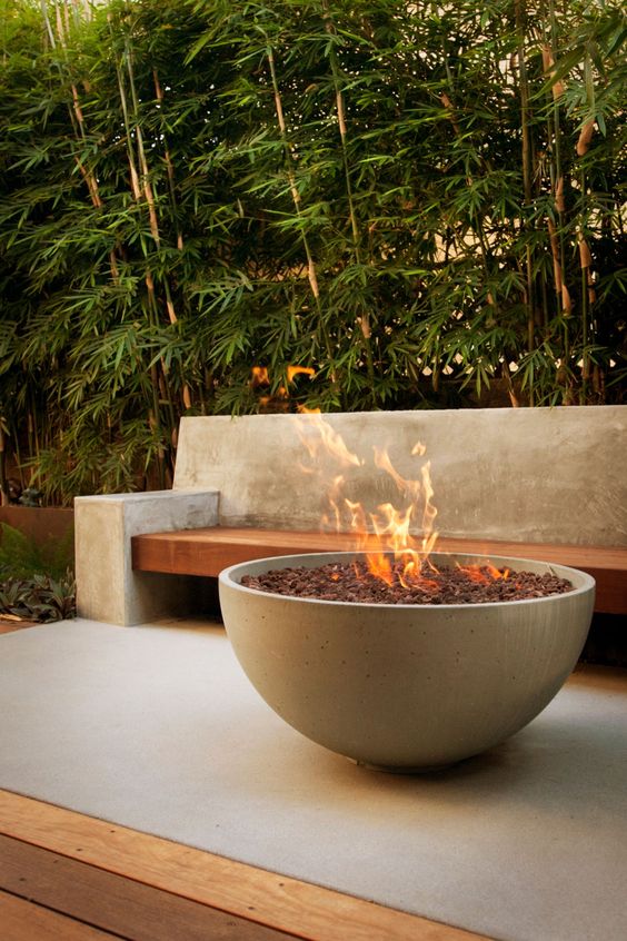 a minimalist outdoor space with a concrete and wood bench, with a large concrete fire pit filled with rocks is amazing