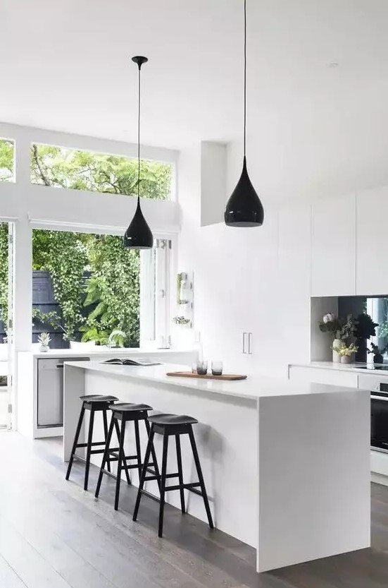 a minimalist white kitchen with several black accents like a backsplash and pendant lamps, stools and fixtures looks airy and bright