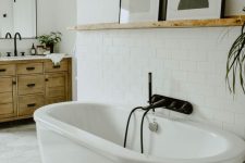 a modern eclectic bathroom with subway and hexagon tiles, an oval tub, a stained vanity and a ledge with art