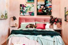 a modern eclectic bedroom with blush textural walls, a pink upholstered bed, colorful bedding, a burgundy pouf, a beaded chandelier and a colorful gallery wall