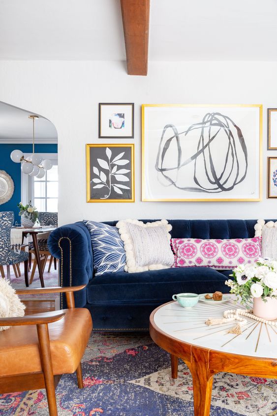 a modern eclectic living room with a navy sofa, amber chairs, a round coffee table, colorful pillows, a free form gallery wall