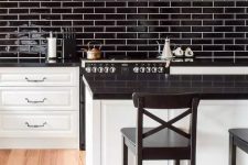a modern farmhouse kitchen with white shaker cabinets and a kitchen island, black countertops, a black skinny tile backsplash and a black hood
