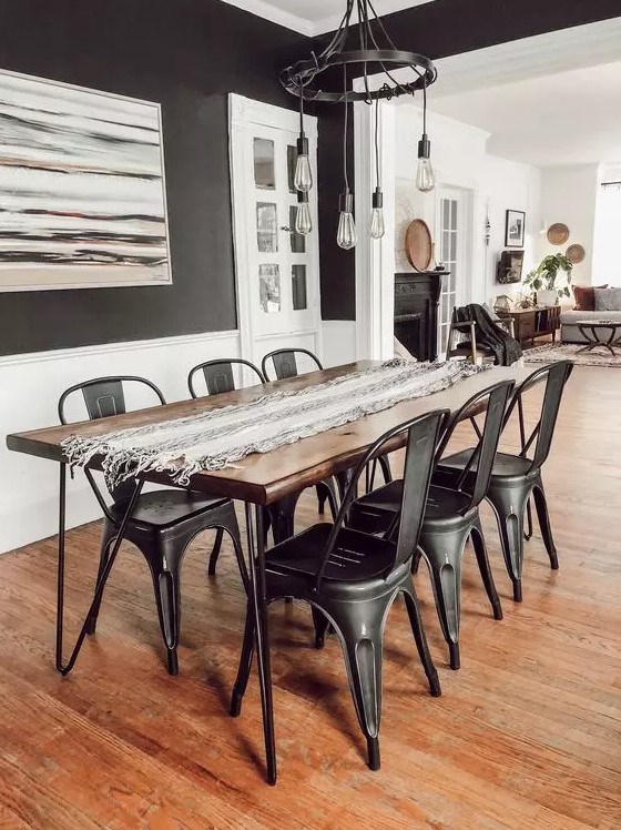 a modern industrial dining room with black walls, a dining table with hairpin legs, black metal chairs and a cool pendant bulb chandelier