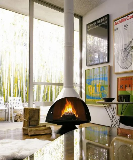 a modern living room with a white Malm fireplace, a bright gallery wall, a glass coffee table and some firewood right on the floor