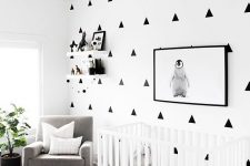 a modern monochromatic nursery with a geo printed wall, a printed rug, a white crib, a grey chair and a potted plant