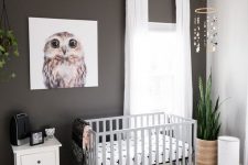 a modern nursery with a black accent wall, a grey crib, potted plants, a printed rug and neutral curtains is very cool