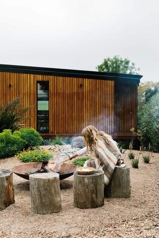 a modern outdoor space with greenery and blooms, with tree stump stools and a wrought iron fire bowl is amazing