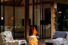 a modern outdoor space with simple wood and metal chairs with pillows, a black metal fire bowl that can be moved