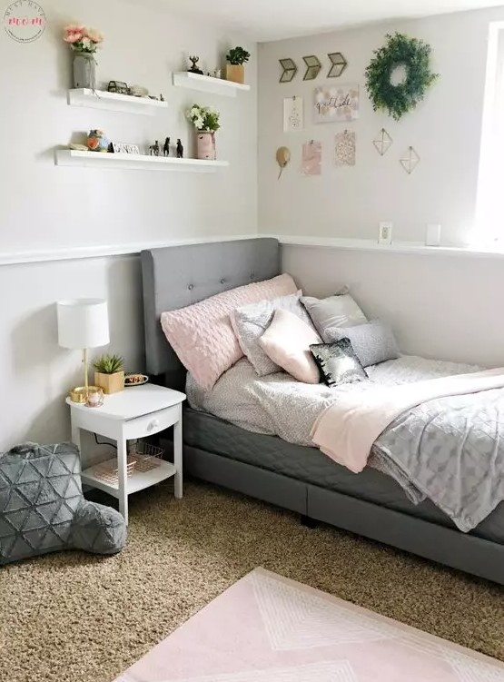 a modern teen bedroom with a grey upholstered bed and pastel bedding, layered rugs, wall-mounted shelves and a greenery wreath