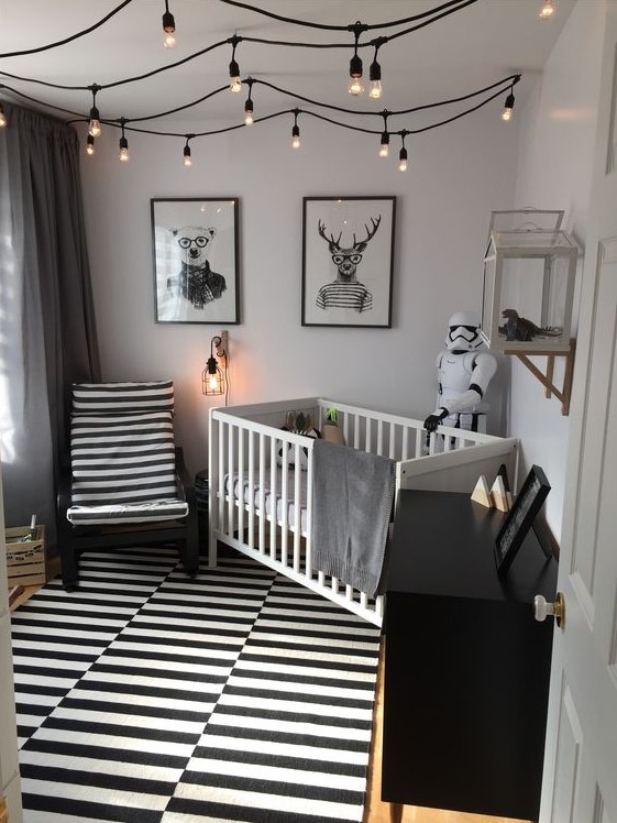 a monochromatic nursery with a striped rug and chair, a black dresser, a white crib and bulbs attached to the ceiling