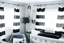 a monochromatic nursery with a white dresser, a white crib and printed black and white textiles and a black chair and a lamp