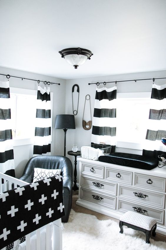 a monochromatic nursery with a white dresser, a white crib and printed black and white textiles and a black chair and a lamp