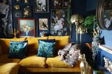 a moody and refined living room with navy walls, a bold yellow sofa, a fireplace with firewood and a round mirror plus gold decor