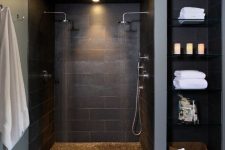 a moody black bathroom with a doorless shared shower space, built-in shelves, a black large scale tile floor and built-in lights