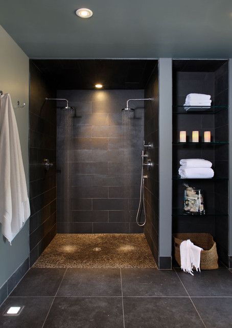 a moody black bathroom with a doorless shared shower space, built-in shelves, a black large scale tile floor and built-in lights
