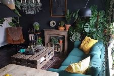 a moody eclectic living space with a teal sofa, a leather chair, colorful pillows, a crystal chandelier and a pallet coffee table