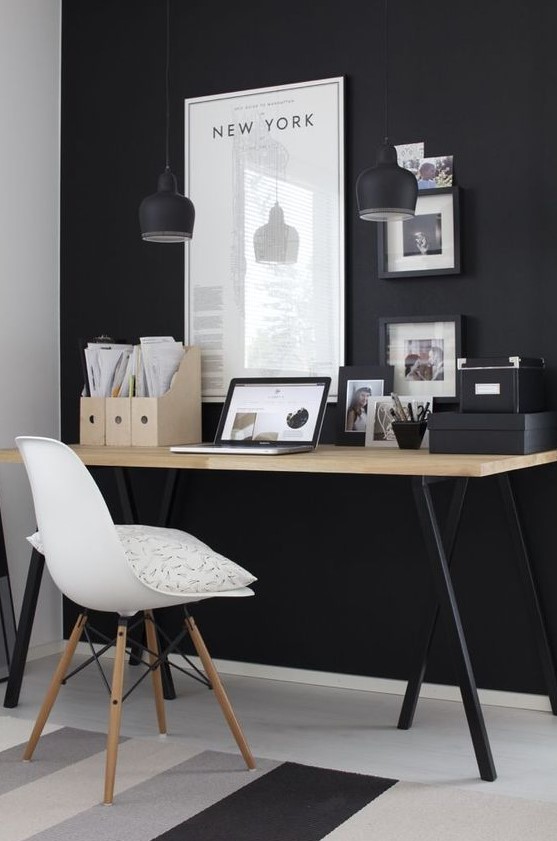 a moody home office with a black statement wall, pendant lamps, a desk with black legs and black framed artworks