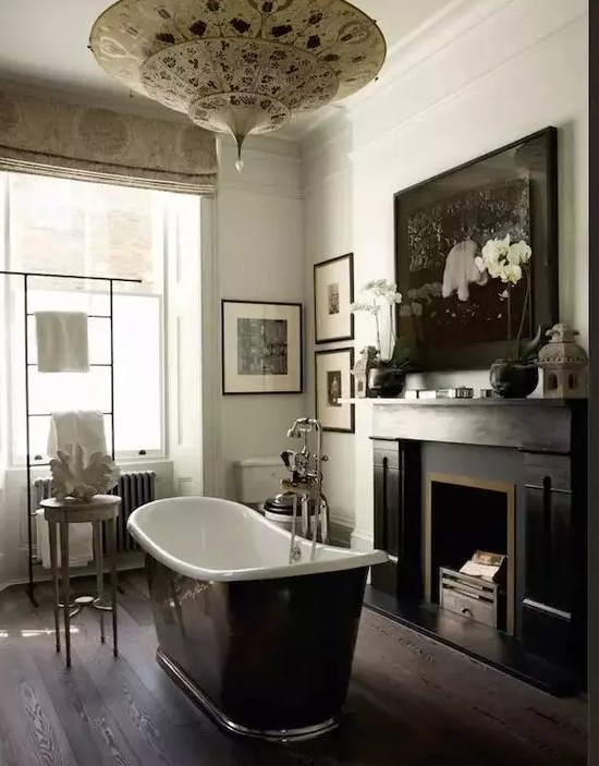 a moody vintage bathroom with a vintage fireplace, a black bathtub, a gallery wall and printed curtains and a printed pendant lamp
