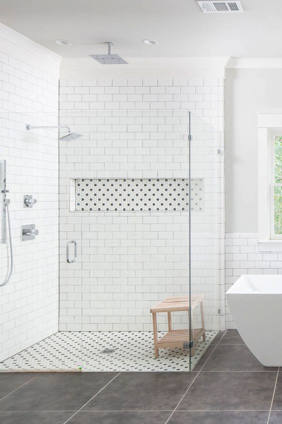 a neutral bathroom with white subway tiles and large scale grey ones, a doorless shower space and a modern bathtub