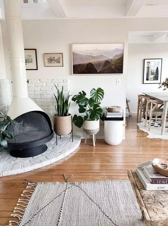 a neutral boho space with a white Malm fireplace, potted plants, a gallery wall, some rugs and lovely modern furniture