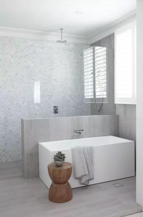 a neutral contemporary bathroom with marble fish scale tiles and a half wall covered with neutral wood plus the same on the floor