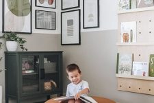 a neutral playroom with a black cabinet, plywood ledges and a corner gallery wall with bright and fun artwork