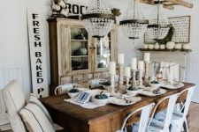 a neutral rustic dining space with a stained buffet, a dark-stained table, white metal chairs and a ladder with crystal chandeliers