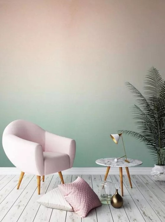 a pastel space with a blush to green gradient accent wall, a blush chair and some pillows, a potted plant and a round table