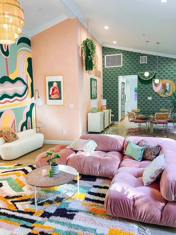 a pretty eclectic living room with coral walls, a bold accent rug, a pink sofa, a coffee table and a bold rug
