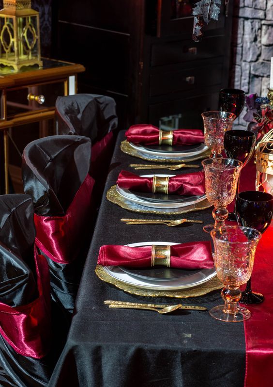 a refined Halloween tablescape with a black tablecloth, a red table runner and napkins, gold chargers and cutlery