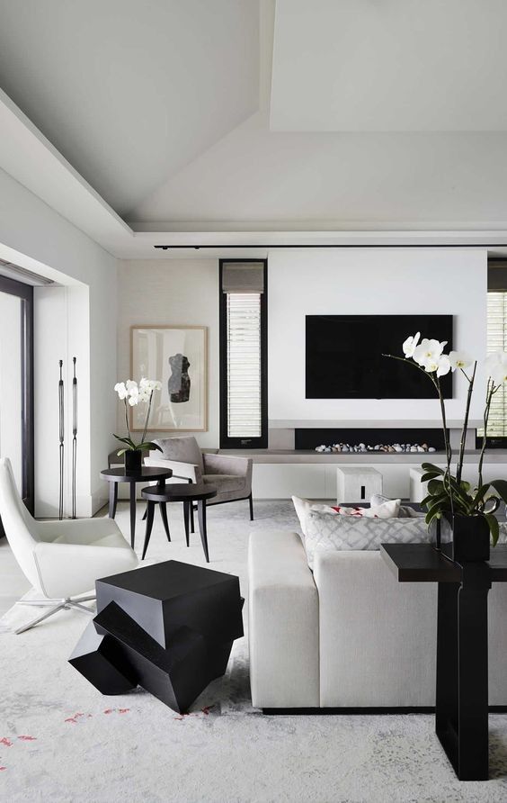 a refined black and white living room with an ethanol fireplace and a TV, neutral furniture, side tables and a catchy black one, artworks