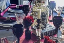 a refined red, black and gold Halloween tablescape with red blooms in black vases, black goblets, a cage, some books and red linens