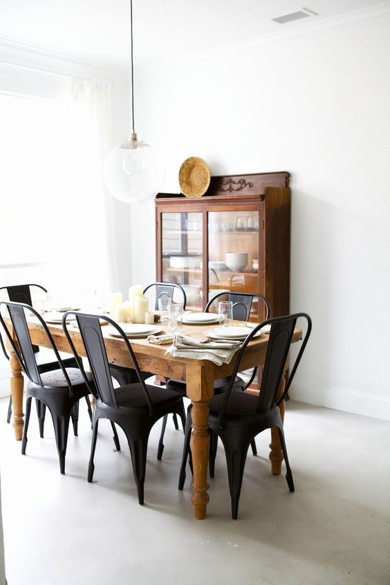 a rustic industrial dining room with a dark-stained buffet, a vintage dining table, black metal chairs, a pendant lamp