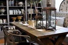 a rustic industrial dining space with a stained trestle table, metal chairs, a chic loveseat and metal pendant lamps, elegant lanterns and greenery