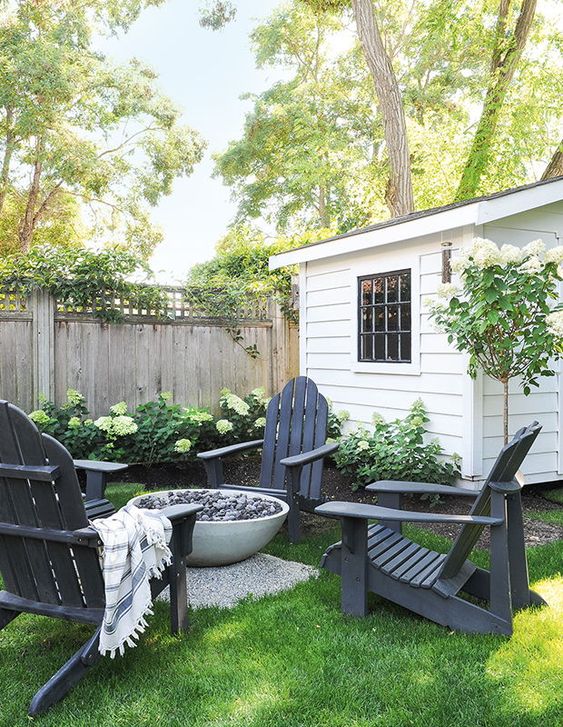 a rustic outdoor space with greenery and blooms, black wooden chairs, a fire bowl in the center is a very welcoming space